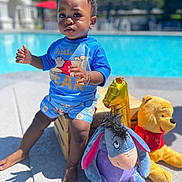 Karson is registered to the contest to win money with this photo: child, toddler, pool, outdoor, sunny, plush_toy, winnie_the_pooh, eeyore, balloon, blue_clothing, shorts, bracelet, barefoot, wooden_crate, concrete, summer, toy, person, expression, daylight