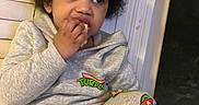 Noah joined the competition — help win amazing prizes! child, toddler, afro_hair, snack, eating, gray_hoodie, pajamas, teenage_mutant_ninja_turtles, indoor, window, curious, sitting, cozy, casual_clothing, portrait, cute, person, young_child, face, hand