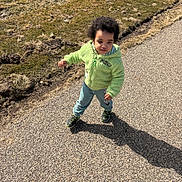 Noah joined the competition — help win amazing prizes! toddler, child, walking, outdoor, path, grass, shadow, green_jacket, curly_hair, casual_clothing, sunlight, pavement, nature, daylight, cute, person, shoes, expression, young_child, casual