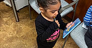 Aaliyah joined the competition — help win amazing prizes! child, girl, lollipop, indoors, reading, card, black_clothing, pink_shoes, hair_bun, office, chair, table, papers, keyboard, floor, curious, standing, focused, toy, young