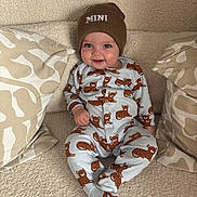 Noah is registered to the contest to win money with this photo: baby, child, infant, smiling, beanie, hat, onesie, bear_pattern, pillow, blanket, soft_texture, cute, happy, indoors, seated, comfortable, cozy, face, clothing, portrait