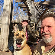 Pasha is registered to the contest to win money with this photo: beard, cap, casual, collar, dog, face, fence, hammock, happy, man, outdoor, person, pet, porch, sky, smiling, sunlight, trees, woman, wood