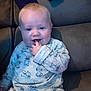 baby, child, pajamas, blue_eyes, sitting, couch, leather, smiling, fingers_in_mouth, cute, indoor, clothing, face, person, infant, young_child, happy, comfort, stitch_pattern, cozy