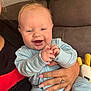 baby, child, infant, smiling, happy, couch, toy, hand, adult, nail_polish, ring, onesie, indoor, person, face, blue_clothing, plush_toy, furniture, closeup, holding