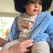 Aylan participe au concours pour gagner de l'argent avec cette photo : adult_hand, baby, blue_jacket, casual, child, clothing, comfort, cute, expression, face, fuzzy_hat, hand, indoor, person, portrait, sitting, soft_light, table, warm_clothes, young_child