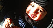 Aylan participe au concours pour gagner de l'argent avec cette photo : baby, child, closeup, cute, face, hand, happy, hat, indoors, infant, knit, person, plush_toy, portrait, shadow, smiling, stroller, sunlight, sweater, warm_clothing