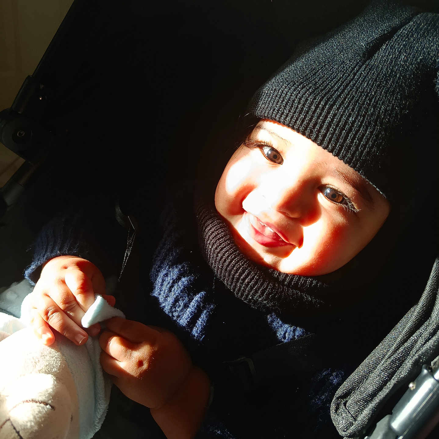 Aylan participe au concours pour gagner de l'argent avec cette photo : baby, child, closeup, cute, face, hand, happy, hat, indoors, infant, knit, person, plush_toy, portrait, shadow, smiling, stroller, sunlight, sweater, warm_clothing