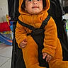 Aylan participe au concours pour gagner de l'argent avec cette photo : baby, bear_costume, black_stroller, child, curious_expression, cute, face, floor_tiles, hood, indoors, orange_onesie, person, plush_clothing, seatbelt, smiling, stroller, toddler, toy, window, young_child