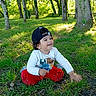 toddler, child, grass, trees, forest, nature, outdoor, cap, clothing, smile, happy, sitting, greenery, daylight, play, young_child, casual, curly_hair, sunlight, park