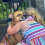 dog, child, hug, embrace, striped_dress, backyard, leash, collar, grill, patio, blond_hair, ponytail, summer, outdoor, close_up, affectionate, pet, mammal, friendship, garden