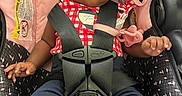 Miorine is registered to the contest to win money with this photo: baby, child, car_seat, infant, beanie, harness, red_checkered_clothing, blue_pants, white_socks, cute, wide_eyes, indoors, seatbelt, safety, pink, black, patterned_fabric, small_hands, portrait, young