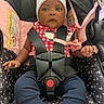 baby, child, car_seat, infant, beanie, harness, red_checkered_clothing, blue_pants, white_socks, cute, wide_eyes, indoors, seatbelt, safety, pink, black, patterned_fabric, small_hands, portrait, young