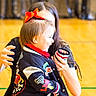 Delilah joined the competition — help win amazing prizes! child, toddler, adult, red_bow, jacket, indoor, gymnasium, floor, hand, smile, person, long_hair, blurred_background, cheerful, holding, clothing, bright_colors, young_child, face, portrait