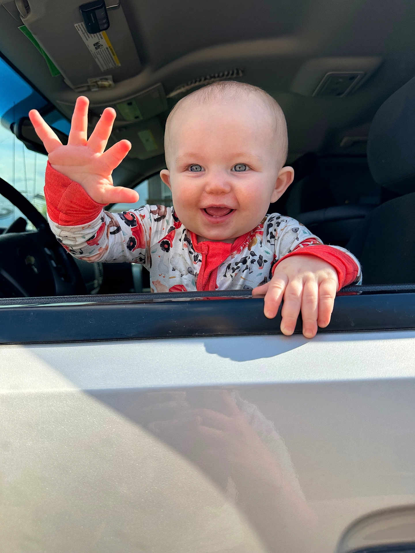 Westyn is registered to the contest to win money with this photo: baby, child, smiling, waving, car, window, onesie, patterned_clothing, blue_eyes, hand, seat, interior, joy, happiness, portrait, infant, cute, daylight, face, person