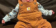 Stetson is registered to the contest to win money with this photo: baby, child, tongue_out, overalls, brown, patterned_shirt, blue_socks, couch, leather, sitting, cute, playful, indoor, infant, smiling, person, small_hands, cozy, portrait, casual