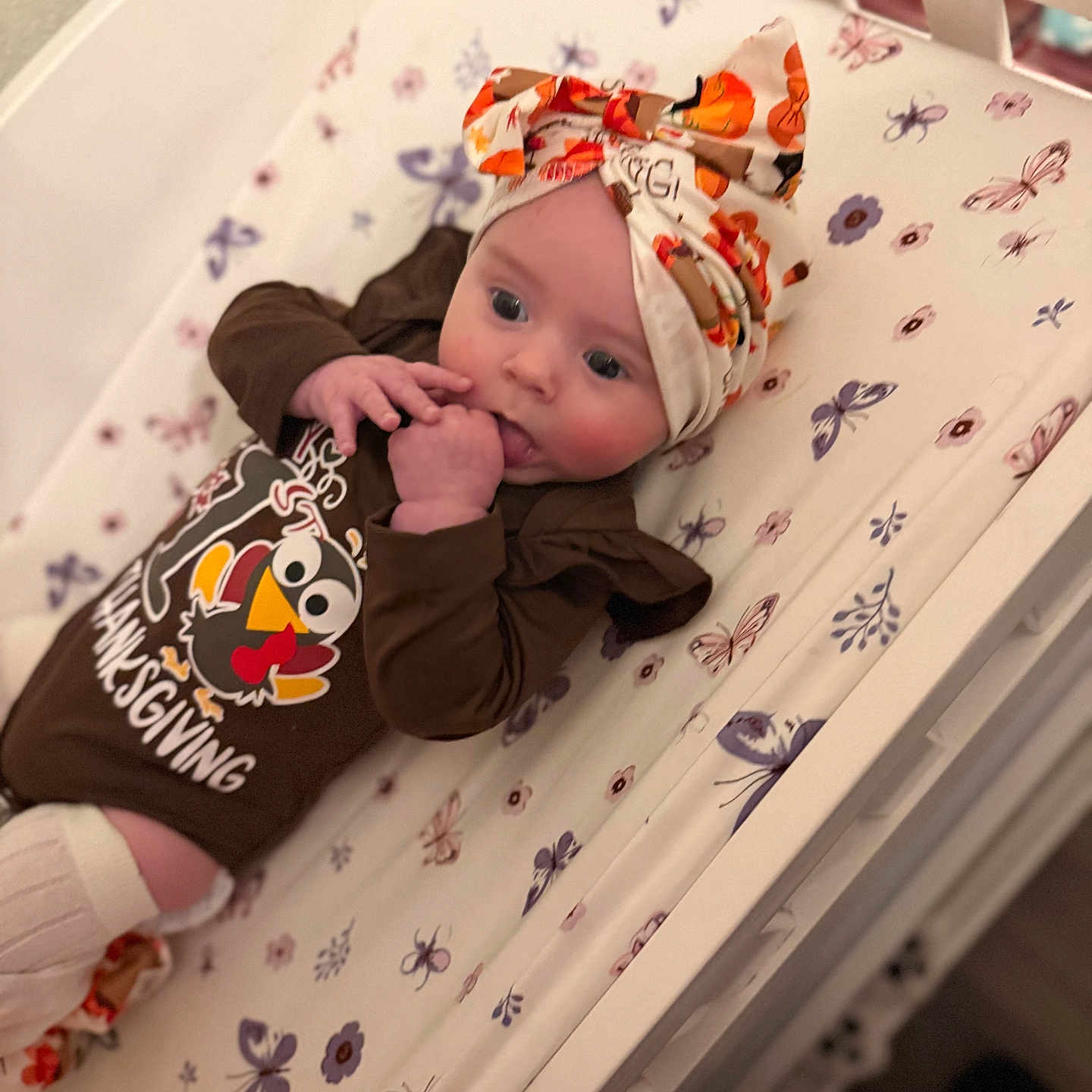 Delylah Rose is registered to the contest to win money with this photo: baby, brown_clothing, butterflies, child, crib, cute, floral, hand_to_mouth, head_wrap, indoors, infant, newborn, pale_skin, patterned_sheet, person, resting, sleeping_area, socks, soft_lighting, thanksgiving