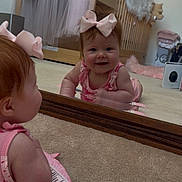 Ember joined the competition — help win amazing prizes! baby, mirror, reflection, pink_bow, smile, tummy_time, nursery, crib, soft_toys, carpet, child, indoor, cute, infant, pink_clothing, headwear, happy, person, room, baby_girl