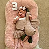 Ember joined the competition — help win amazing prizes! baby, infant, smiling, pink_cushion, plush_toy, goose, bow, carpet, white_shirt, floral_outfit, cute, child, happy, lying_down, soft_texture, indoors, number_three, headband, person, portrait