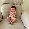 baby, child, infant, smiling, sitting, chair, cushion, onesie, floral_pattern, hair, happy, indoors, face, cute, skin, feet, arms, legs, person, furniture