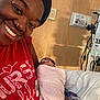 Riley is registered to the contest to win money with this photo: person, smile, baby, newborn, hospital, medical_equipment, blanket, bed, tubes, healthcare, face, headwear, red_shirt, indoor, care, love, patient, nurture, happy, mother