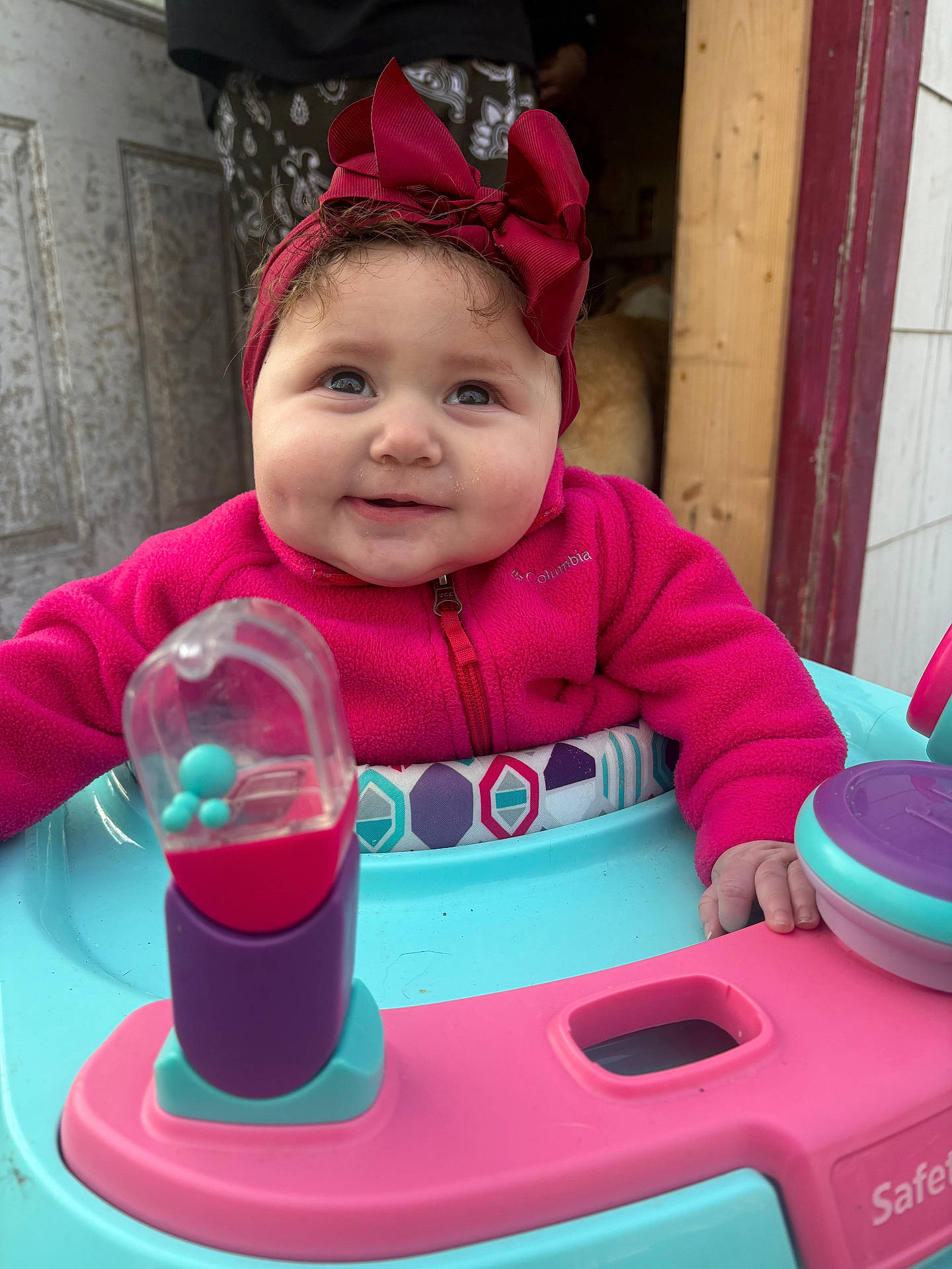 Evelynn joined the competition — help win amazing prizes! baby, baby_walker, casual_clothing, child, chubby_cheeks, closeup, colorful, cute, furniture, happy, headband, indoor, infant, person, pink_jacket, playful, portrait, smiling, toy, wooden_door