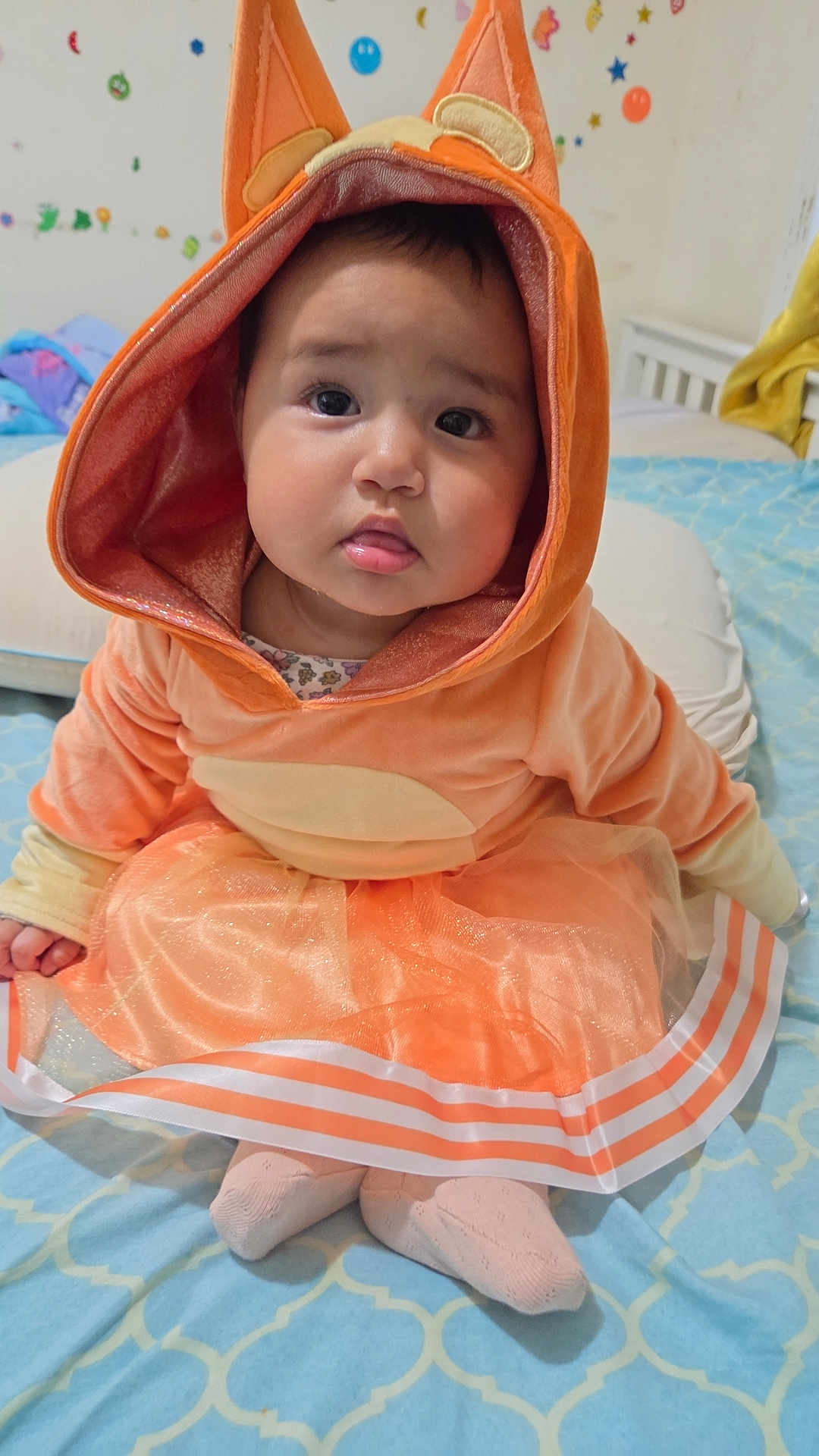 Luna joined the competition — help win amazing prizes! baby, child, orange_costume, hood, ears, bed, blanket, blue, pattern, tulle_skirt, socks, cute, indoor, portrait, toddler, face, expression, soft, home, cozy