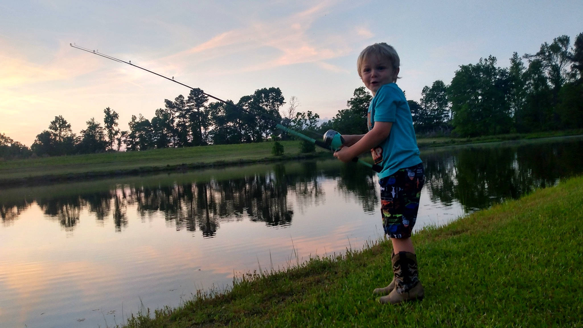 Cam is registered to the contest to win money with this photo: angling, bank, cloud, grass, happy, lake, landscape, leisure, morning, natural_environment, natural_landscape, people_in_nature, person, plant, shorts, sky, sunlight, toddler, tree, water