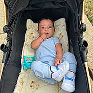 Michael joined the competition — help win amazing prizes! baby, stroller, blanket, toy, footwear, blue_clothing, infant, outdoor, curious, hand, face, person, cute, teddy_bear_pattern, sneakers, baby_clothes, child, small_toy, cushion