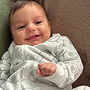 Milo a rejoint le concours — aidez-le/la à gagner de superbes lots ! baby, smiling, face, infant, clothing, white_outfit, elephant_print, hand, soft_surface, brown_background, cute, cozy, portrait, young_child, fingertip, relaxed, indoors, cute_baby, happy, child