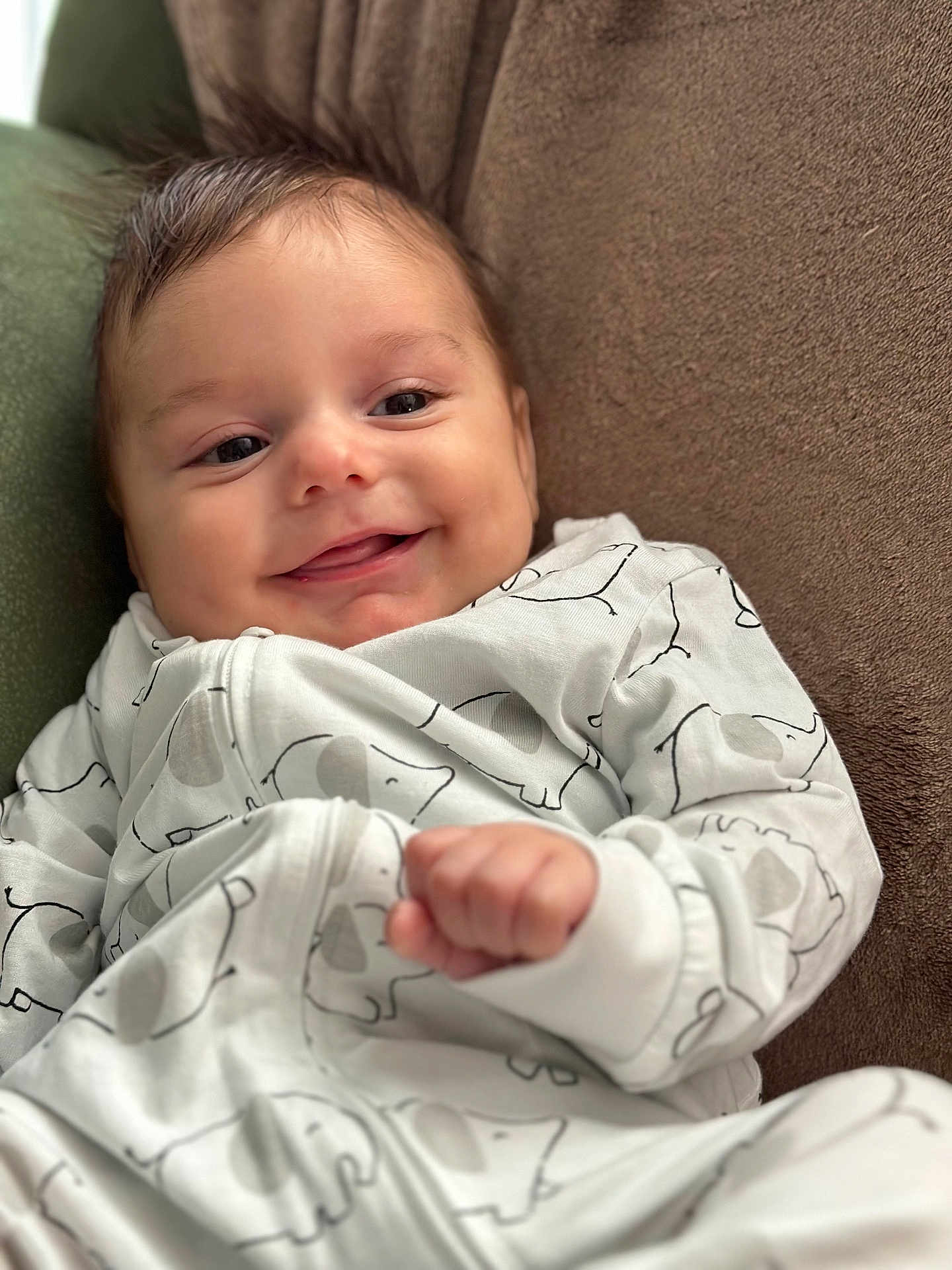 Milo a rejoint le concours — aidez-le/la à gagner de superbes lots ! baby, smiling, face, infant, clothing, white_outfit, elephant_print, hand, soft_surface, brown_background, cute, cozy, portrait, young_child, fingertip, relaxed, indoors, cute_baby, happy, child