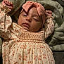 baby, infant, sleepy, headband, bow, blanket, floral_dress, arms_up, indoors, soft_texture, cute, child, portrait, relaxed, cozy, sleepwear, skin, face, young, person