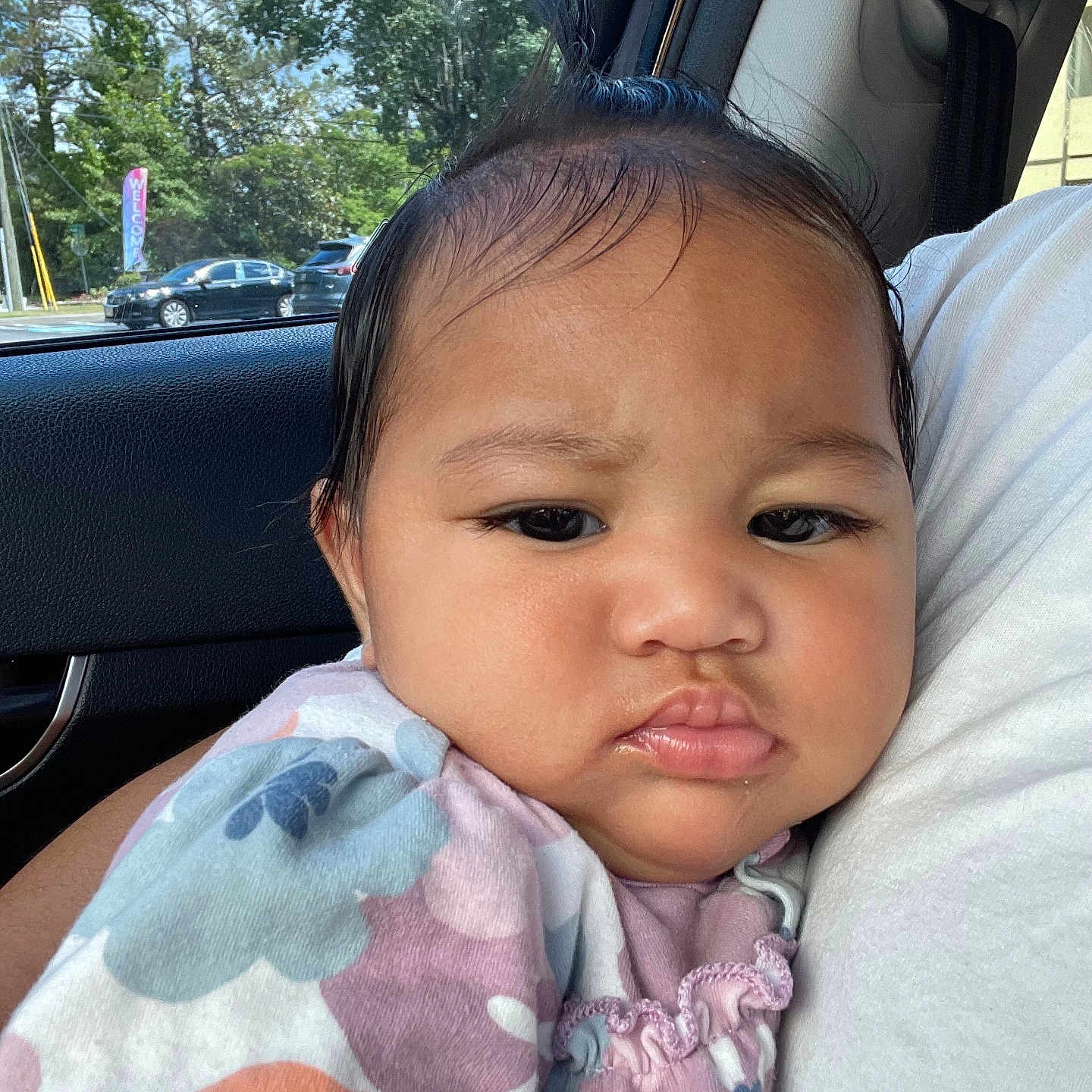 Amarah-Jayne is registered to the contest to win money with this photo: baby, car_interior, cheeks, child, clothing, daylight, expression, eyebrows, face, flower_pattern, hair, holding, indoors, lips, person, portrait, seat, skin, trees, window