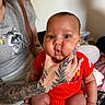 Maveriq joined the competition — help win amazing prizes! adult, baby, casual, child, cute, expression, face, hand, indoor, jewelry, long_hair, nail_art, person, portrait, pout, red_clothing, sitting, skin, tattoo, tshirt