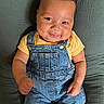 baby, blanket, cheeks, child, clothing, cute, denim_overalls, eyes, face, hands, happy, head, indoors, infant, person, portrait, sitting, skin, smile, yellow_shirt