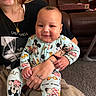 Maveriq is registered to the contest to win money with this photo: adult, baby, black_shirt, carpet, child, clothing, couch, face, hand, happy, head, indoor, living_room, mickey_mouse, onesie, person, pizza_box, sitting, smile, tattoo