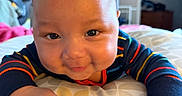 Maveriq is registered to the contest to win money with this photo: baby, bed, cheeks, child, closeup, cute, face, hands, happy, home, indoor, infant, lying_down, mattress, person, portrait, skin, smiling, striped_clothing, young