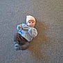 baby, infant, carpet, hat, sweater, blue, brown_pants, socks, lying_down, indoor, cute, child, person, shadow, texture, knitwear, cozy, expression, playful, floor