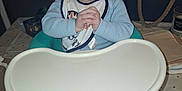 Wesley is registered to the contest to win money with this photo: baby, bib, baby_chair, tray, table, feet, hands, face, expression, indoor, person, child, clothing, high_chair, tablecloth, bag, candle, napkin, curious, infant