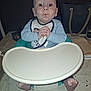 baby, bib, baby_chair, tray, table, feet, hands, face, expression, indoor, person, child, clothing, high_chair, tablecloth, bag, candle, napkin, curious, infant