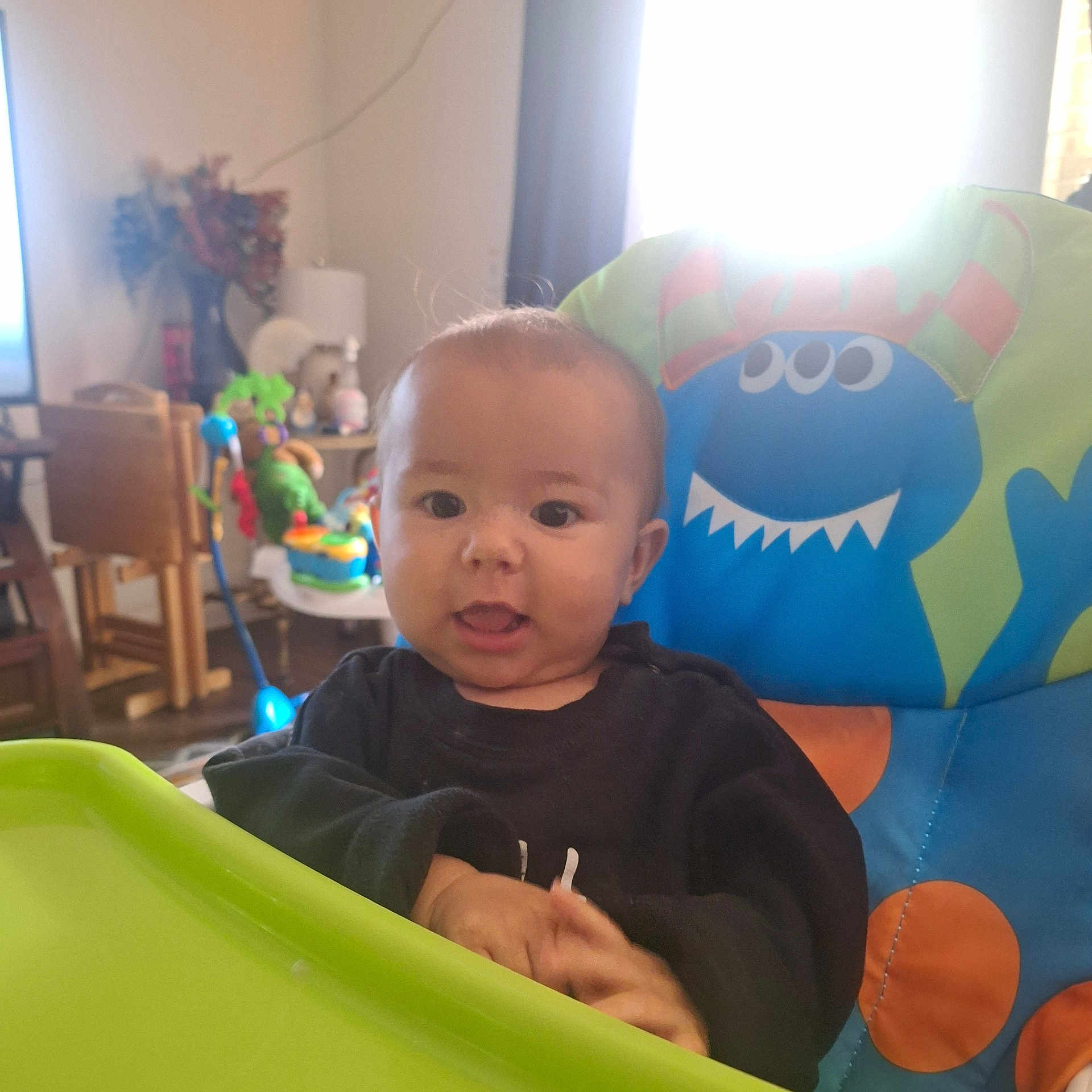 Elijah joined the competition — help win amazing prizes! baby, blue_monster, child, clothing, colorful, curious_expression, face, furniture, hands, high_chair, home, indoor, light, living_room, person, seat, smile, table, toy, window