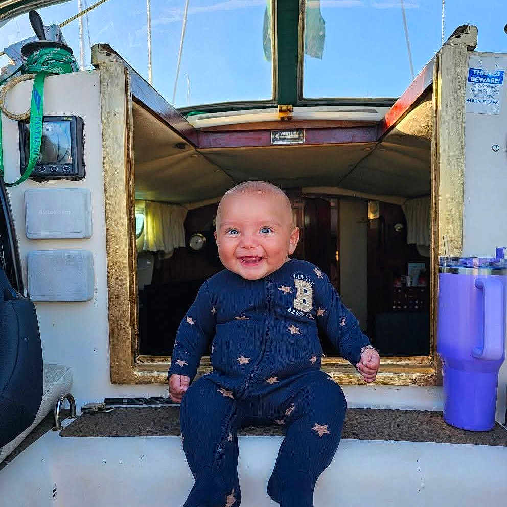 Danny is registered to the contest to win money with this photo: baby, blue_eyes, boat, cabin, child, doorway, happy, indoor, interior, nautical, onesie, purple, rope, seat, sitting, smiling, star_pattern, tumbler, window, wood