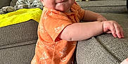 Owen is registered to the contest to win money with this photo: baby, child, orange_shirt, diaper, couch, carpet, living_room, smile, standing, grip, cheeks, eyes, blanket, furniture, person, indoor, home, cute, toddler, playful