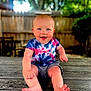 Owen joined the competition — help win amazing prizes! baby, child, smiling, outdoor, tie_dye_shirt, shorts, barefoot, wooden_deck, fence, greenery, sunlight, happy, cute, portrait, young_child, sitting, nature, daylight, face, skin