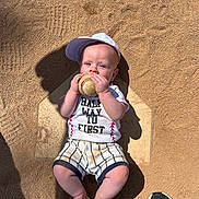 Owen is registered to the contest to win money with this photo: baby, baseball, cap, child, sportswear, home_plate, sand, shadow, sneaker, outdoor, sunlight, cute, infant, grip, shorts, shirt, play, ball, feet, person