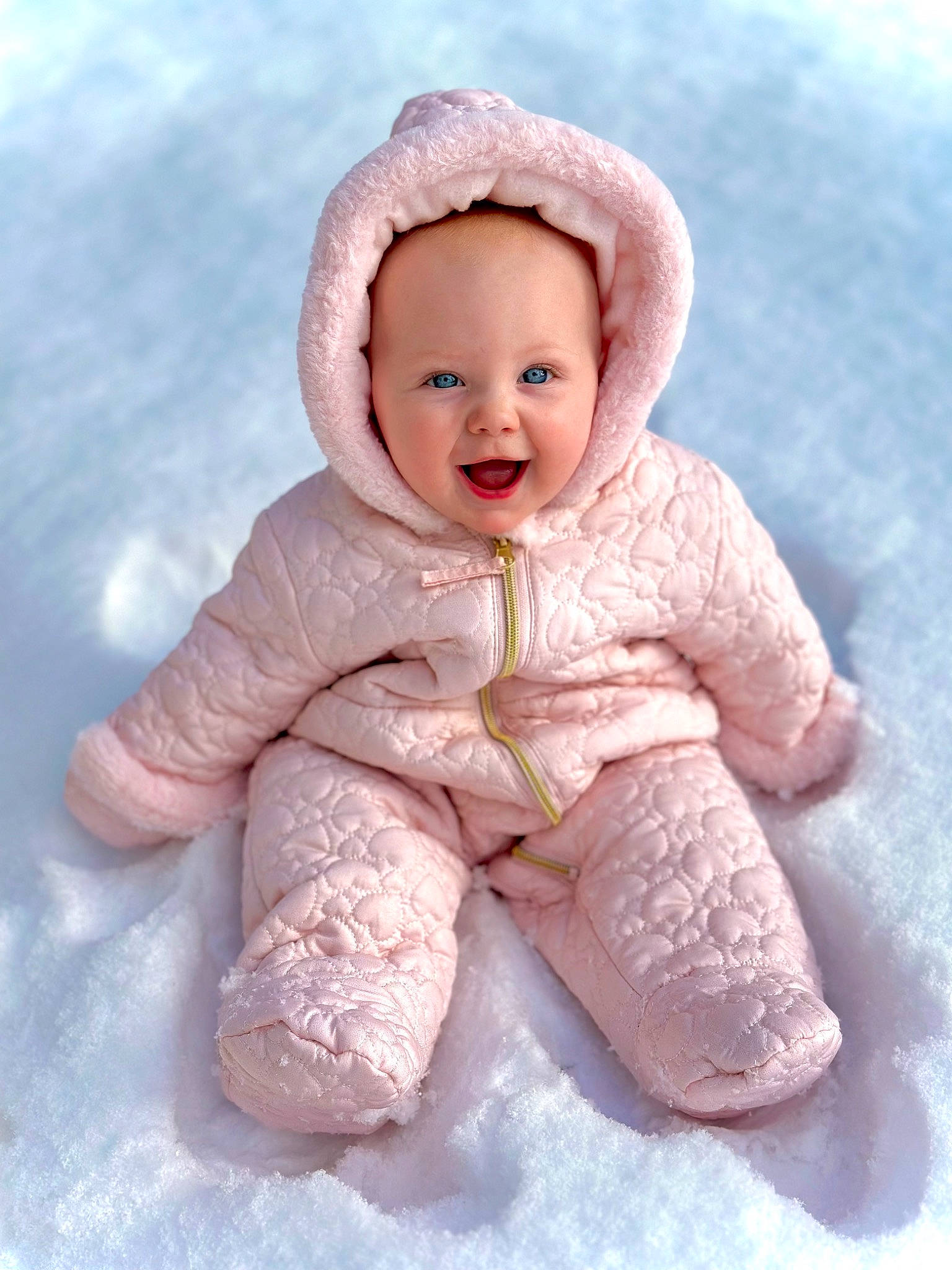 Kora is registered to the contest to win money with this photo: arm, baby, baby_toddler_clothing, cheek, eye, face, gesture, happy, head, human_body, nose, outerwear, person, pink, skin, sleeve, smile, snow, thumb, toddler