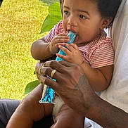 Aulani is registered to the contest to win money with this photo: baby, child, adult, hand, tattoo, frozen_treat, blue, striped_shirt, diaper, sitting, outdoor, greenery, mesh_screen, summer, refreshment, cute, portrait, skin, people, relaxation