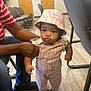 Aulani is registered to the contest to win money with this photo: toddler, child, indoor, floor, wooden_floor, hat, striped_clothing, pink, white, shoes, adult_hand, supporting, door, chair, person, curious_expression, casual, jeans, seated_adult, waiting_room