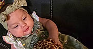 Zoe joined the competition — help win amazing prizes! baby, child, comfortable, couch, curious, cute, giraffe_pattern, green_dress, headband, indoors, infant, leather, person, playful, plush_toy, portrait, seated, smile, soft_toy, young_child