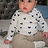 baby, bed, child, clothing, cute, eyes, face, headboard, heart_pattern, indoor, infant, long_sleeve_shirt, pants, person, pillow, portrait, quilt, sitting, skin, sock