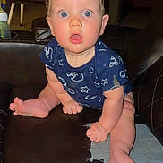 Sebastian is registered to the contest to win money with this photo: baby, child, infant, dribble, blue_eyes, onesie, sitting, leather_couch, indoor, curious, wide_eyes, clothing, foot, hand, face, expression, young, furniture, home, casual